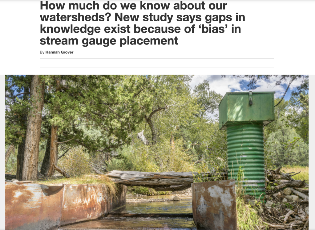 Photo of a stream gauging instrument in a small stream channel. The stream is flowing between a small metal channel next to which a green structure contains the gauging infrastructure.
