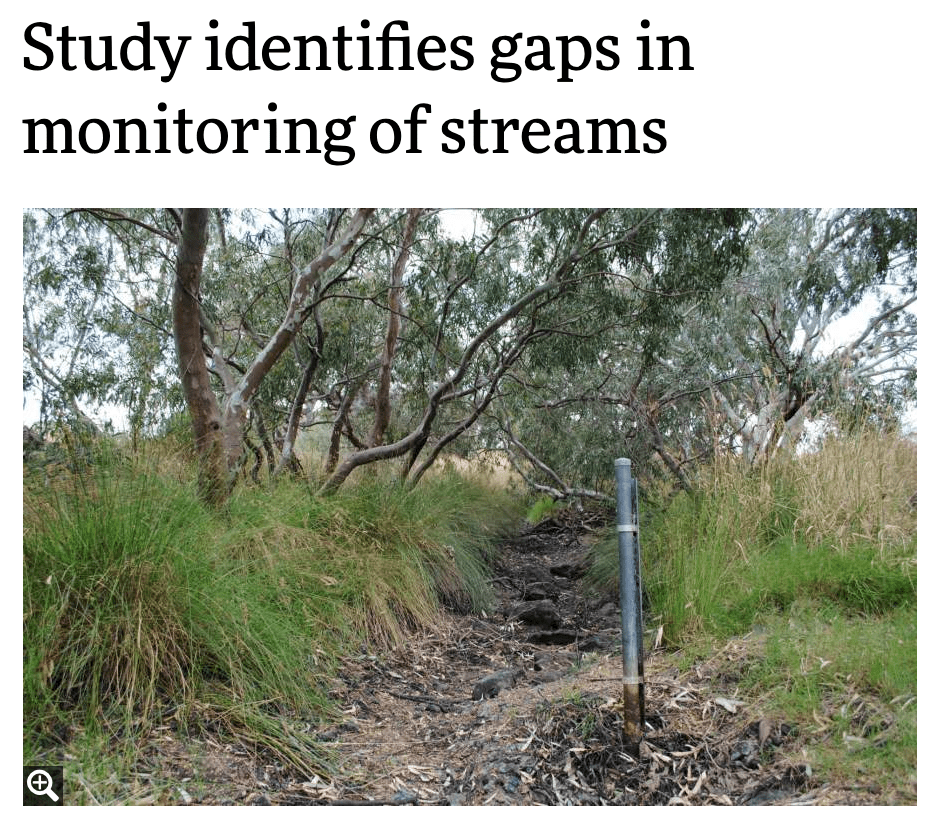 Photo of a dry stream bed that has a stream gauge placed near the center of the small channel. The gauge is a metal pole with a measuring tool attached.